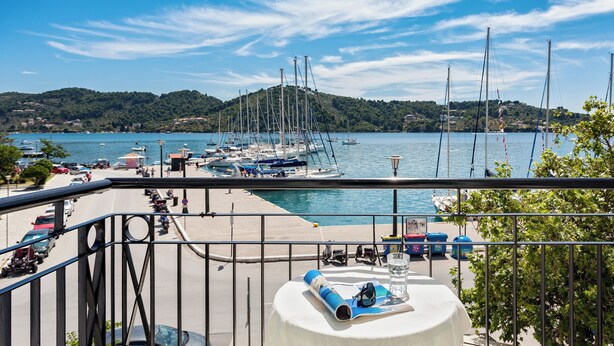 A balcony with a table, a view of a marina with boats, and a hilly landscape in the background. - Akti (Skiathos)