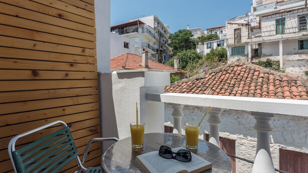 A balcony with a wooden wall, a green chair, a table with a book and glasses, and two glasses of orange juice. - Akti (Skiathos)
