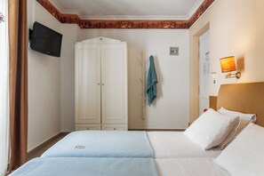 Une chambre d’hôtel comprenant un lit, une armoire, un téléviseur fixé au mur et une lampe également fixée au mur.