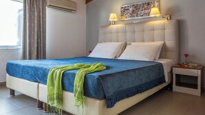 A bedroom with a large bed, two bedside lamps, a nightstand, and a window with curtains. - Akti (Skiathos)