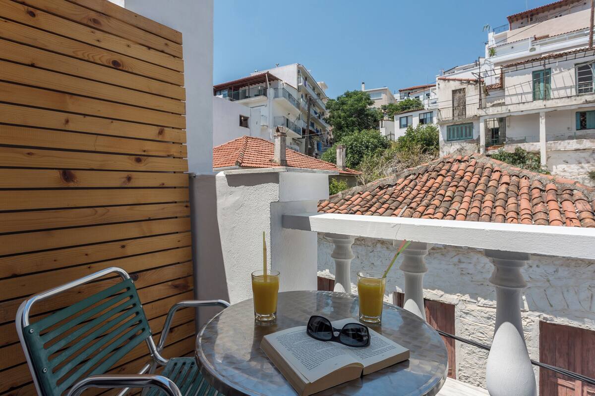 A balcony with a wooden wall, a green chair, a table with a book and glasses, and two glasses of orange juice.
