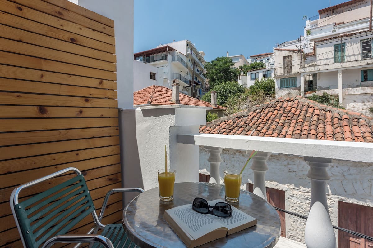 Un balcon avec un mur en bois, une chaise verte, une table avec des boissons et des lunettes de soleil, et un livre.