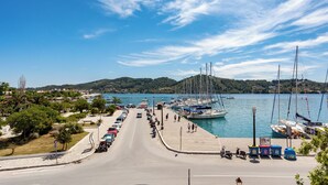 A marina with boats docked, a road leading to the water, and a hilly landscape in the background. - Akti (Skiathos)