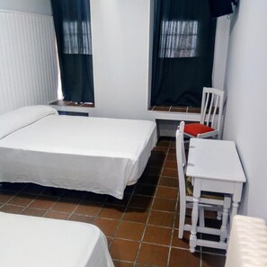 Een kleine, eenvoudige kamer met twee bedden, een stoel, een tafel en een raam met gordijnen.