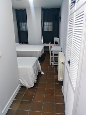 Een kleine kamer met twee bedden, een stoel en een radiator.