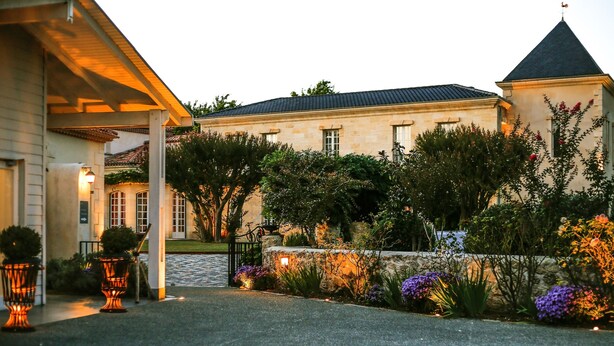 A stone building with a covered entrance and a garden with various plants and flowers. - Domaine de Larchey & son restaurant - Bordeaux Sud (Saint-Medard-d'Eyrans)
