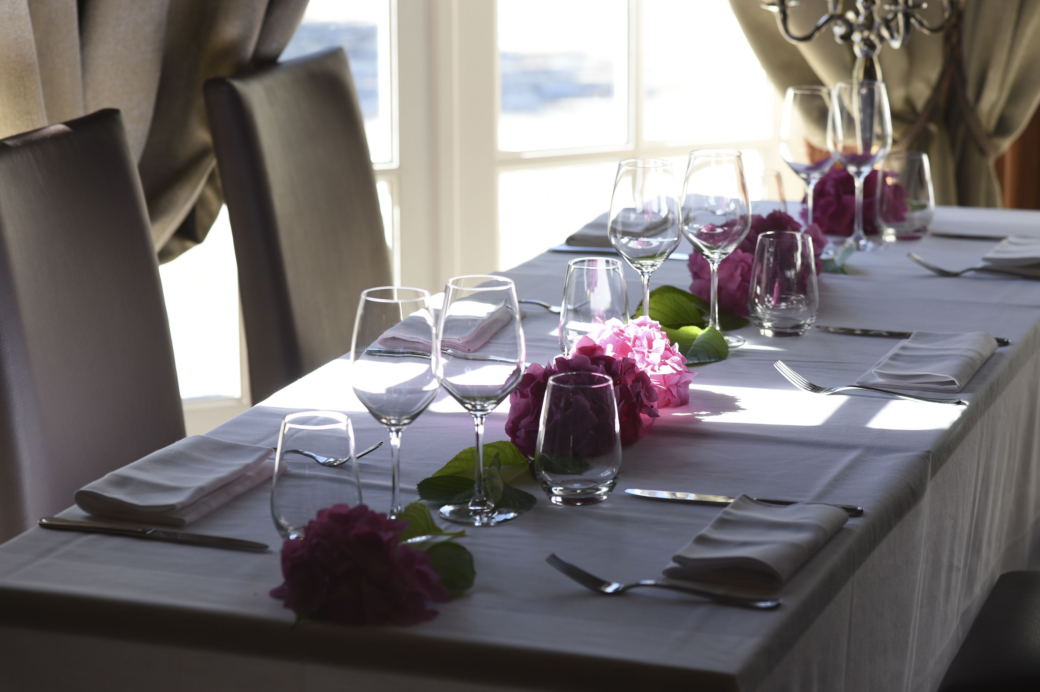 A table set for dining with multiple wine glasses, cutlery, and pink flowers.