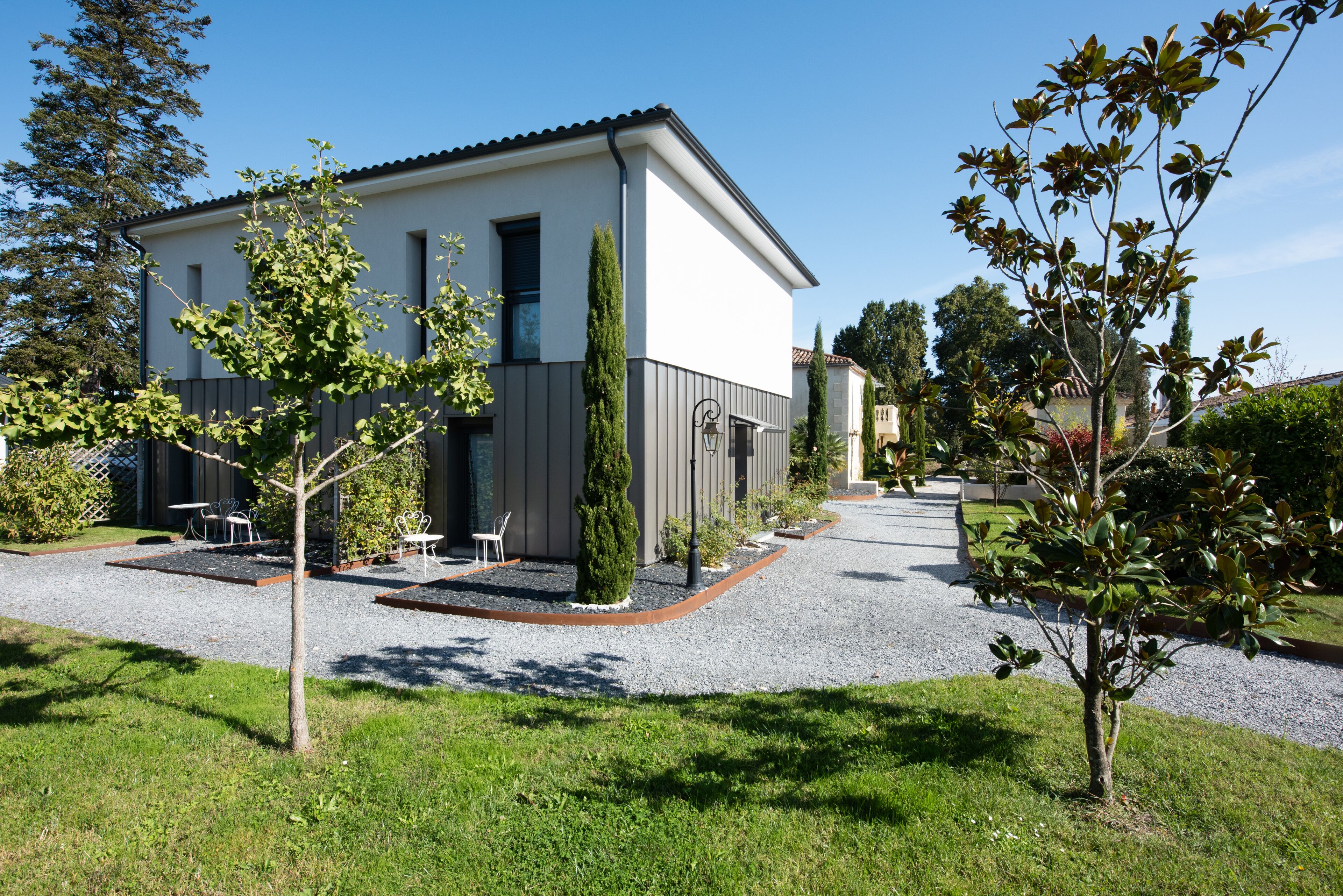 Une maison moderne à deux étages, dotée d’une allée en gravier et entourée de pelouses et d’arbres bien entretenus.