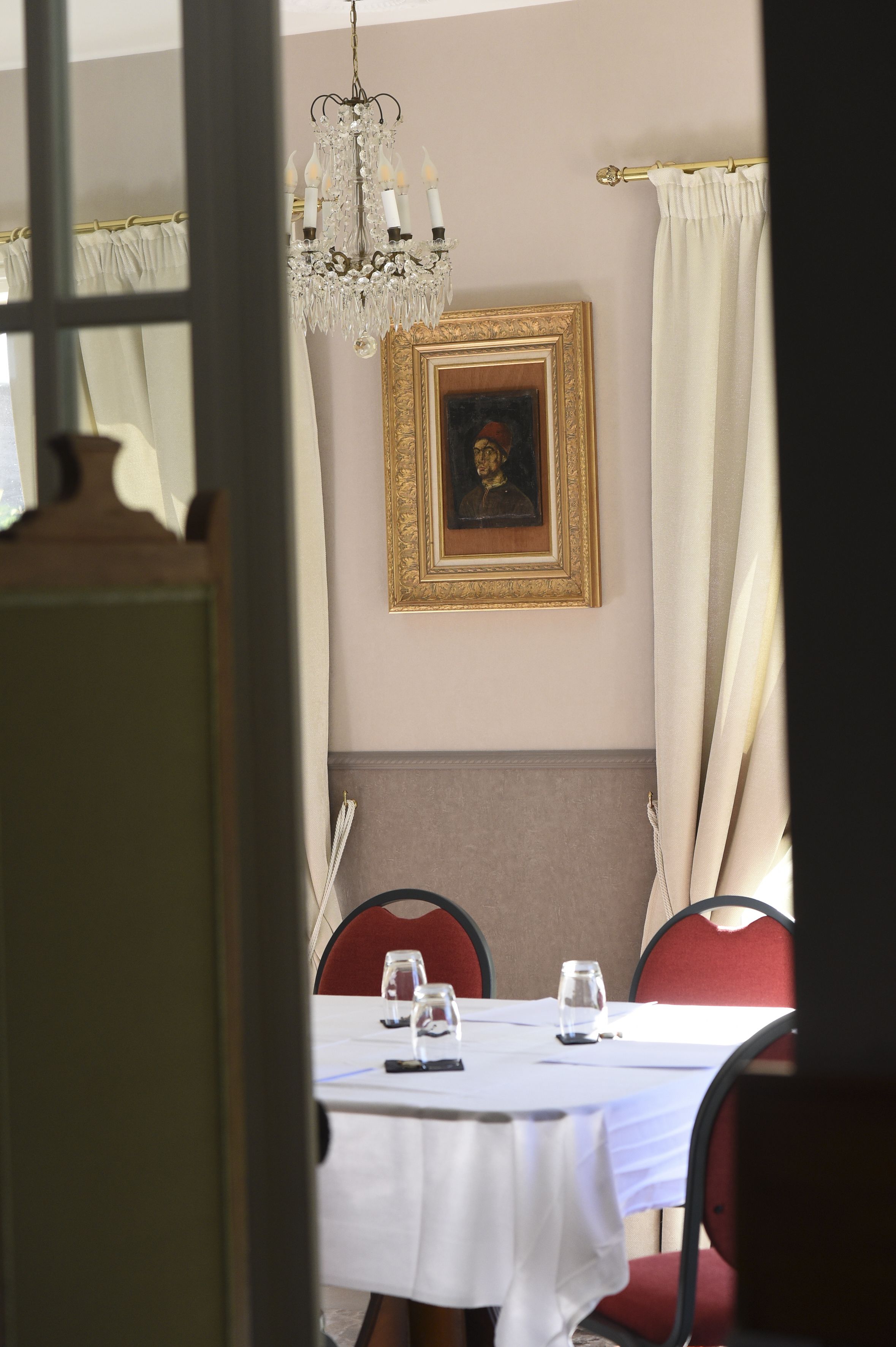 Un comedor con una mesa dispuesta para dos, una araña y un retrato enmarcado en la pared.