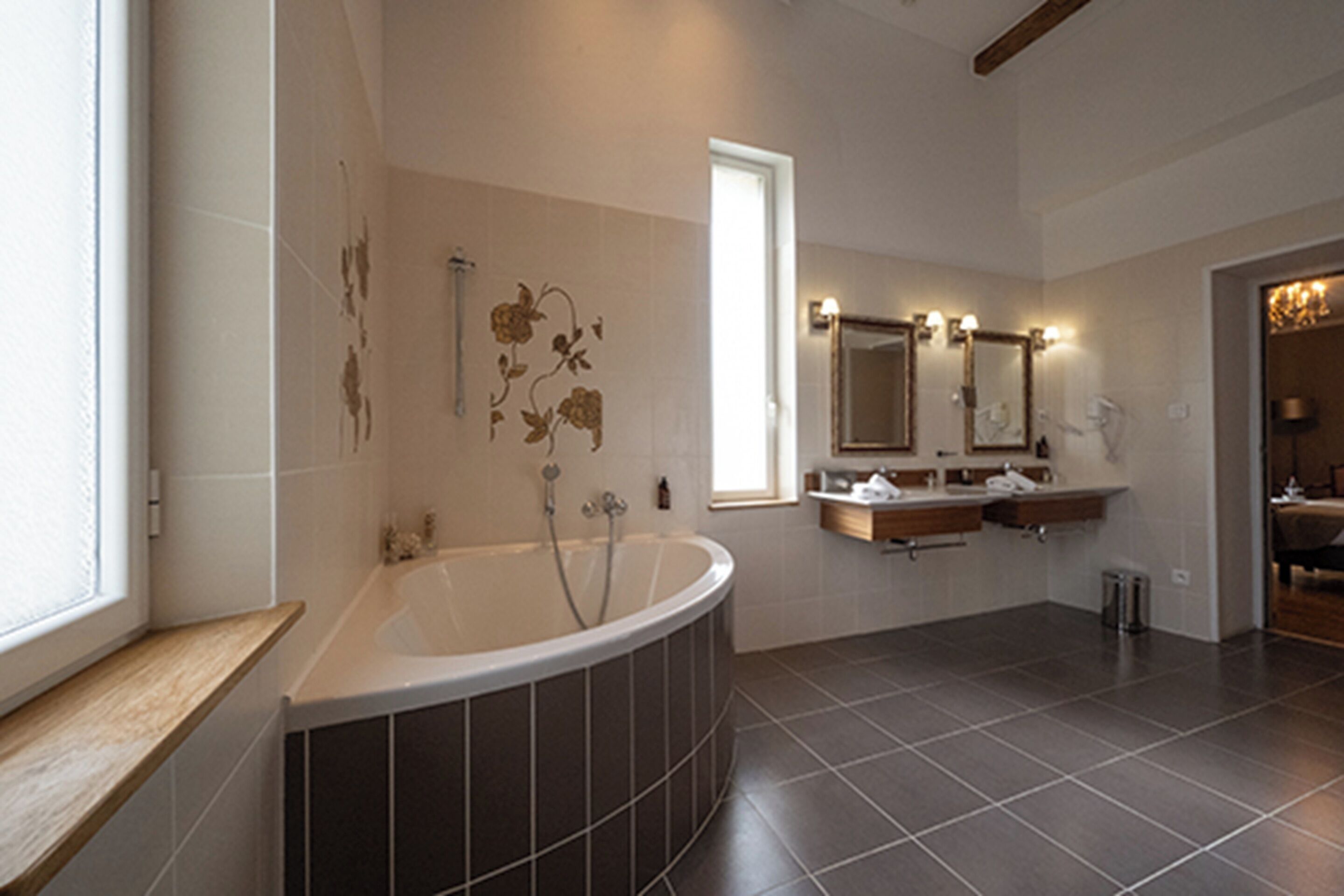 A modern bathroom with a freestanding bathtub, a double vanity with mirrors, and a large window providing natural light.