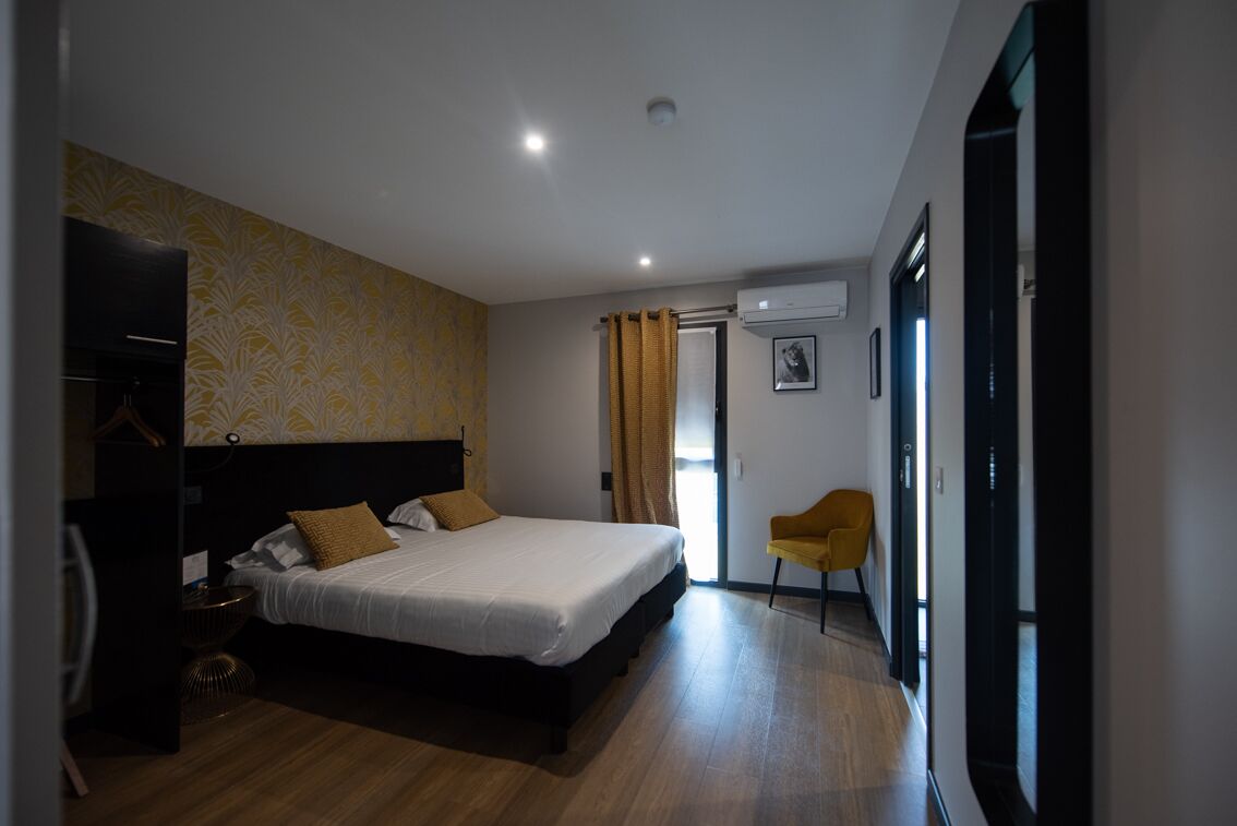 A modern hotel room with a large bed, a wardrobe, a desk, and a chair.