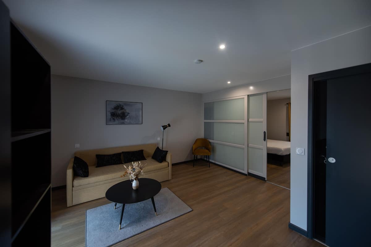 Una sala moderna con un sofá, una mesa de centro y una silla. Hay una puerta corrediza que da a un dormitorio.