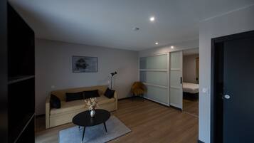 Una sala moderna con un sofá, una mesa de centro y una silla. Hay una puerta corrediza que da a un dormitorio.