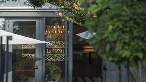 An outdoor seating area with tables and chairs, a glass door entrance, and a decorative plant with pink flowers. - Domaine de Larchey & son restaurant - Bordeaux Sud (Saint-Medard-d'Eyrans)