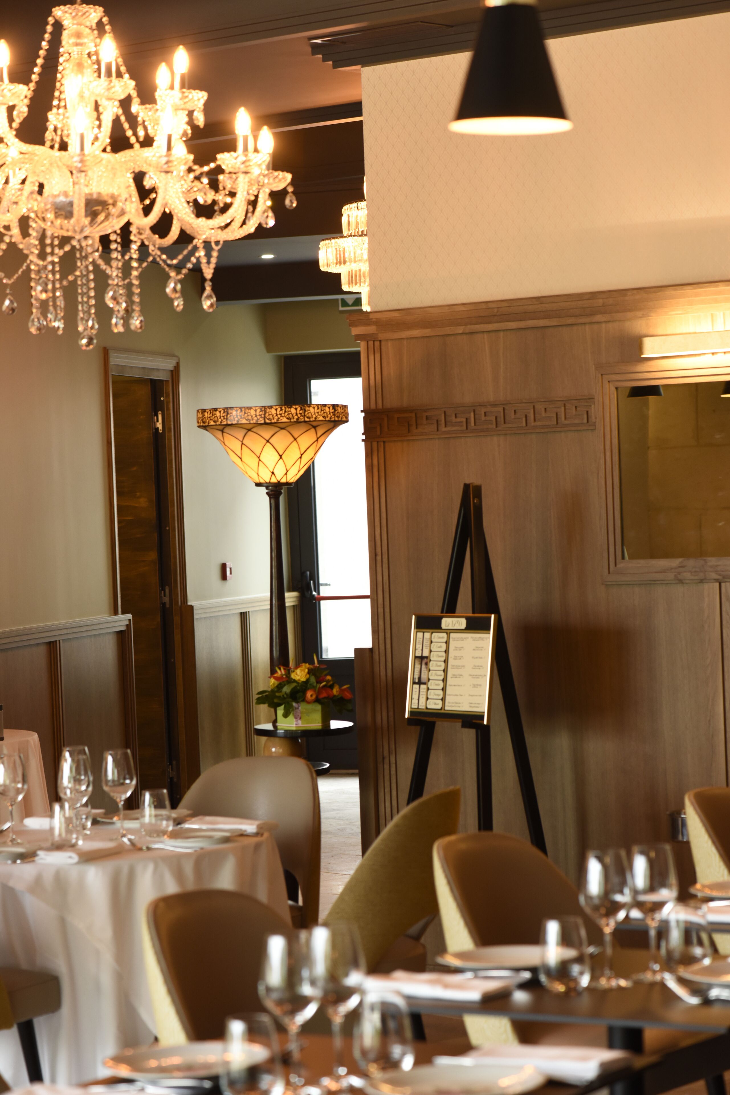 A dining area with tables set for service, a chandelier, and a large floor lamp.