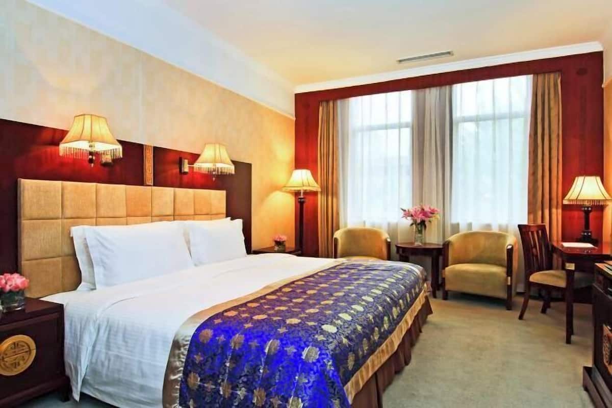 Habitación de hotel con una cama grande, dos lámparas de noche, un escritorio, una silla y una ventana con cortinas.