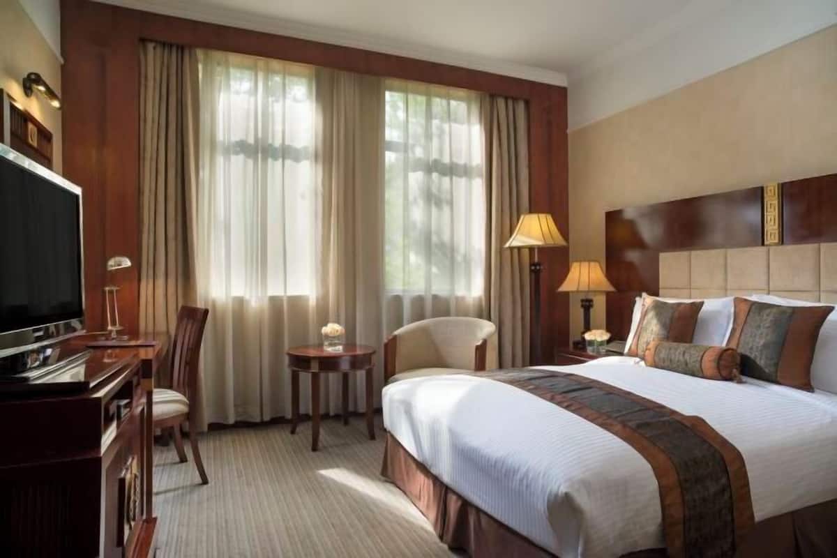 Habitación de hotel con cama, televisor, escritorio, silla, lámpara y cortinas.