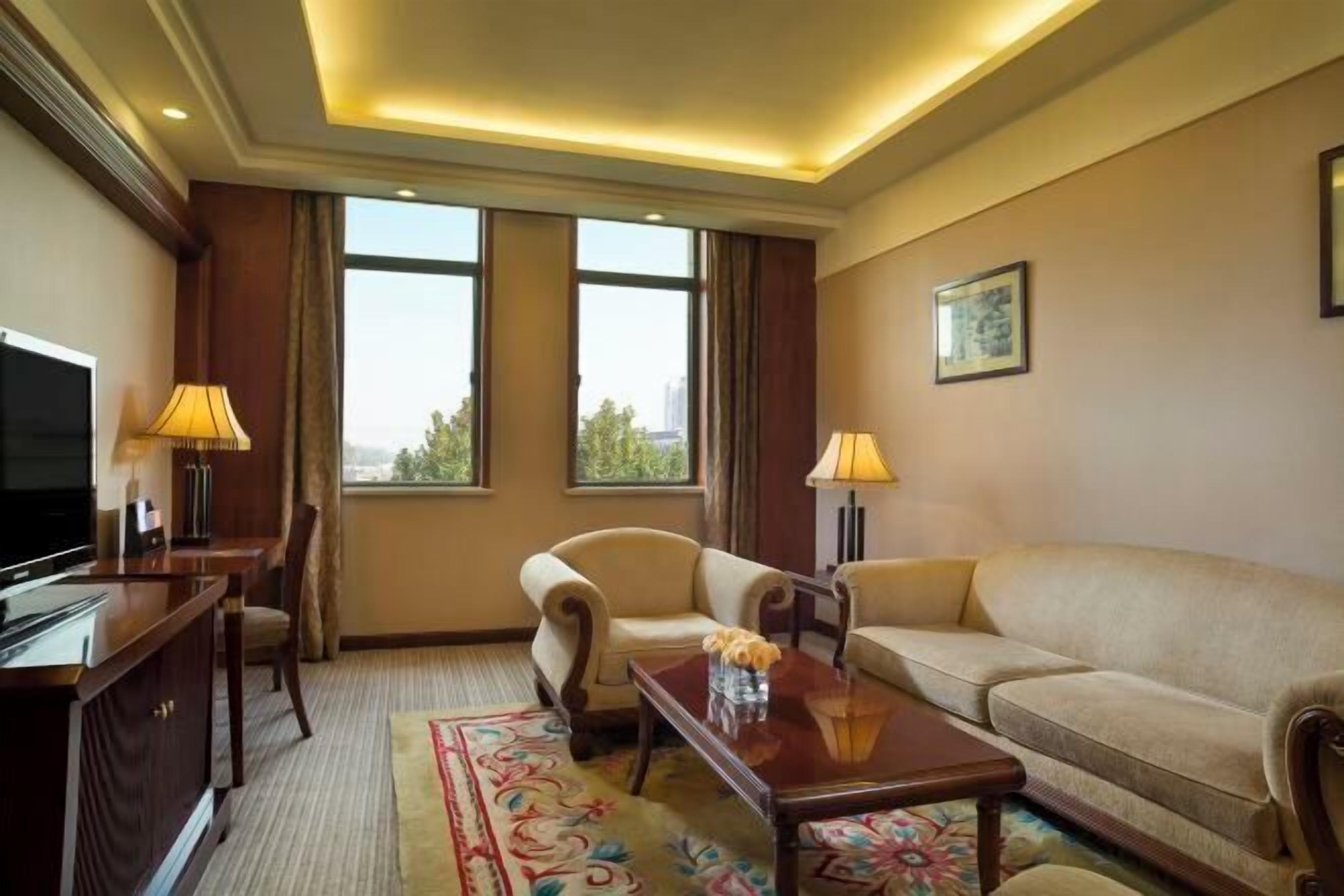 A hotel room with a large window, a sofa, a chair, a desk, and a television.