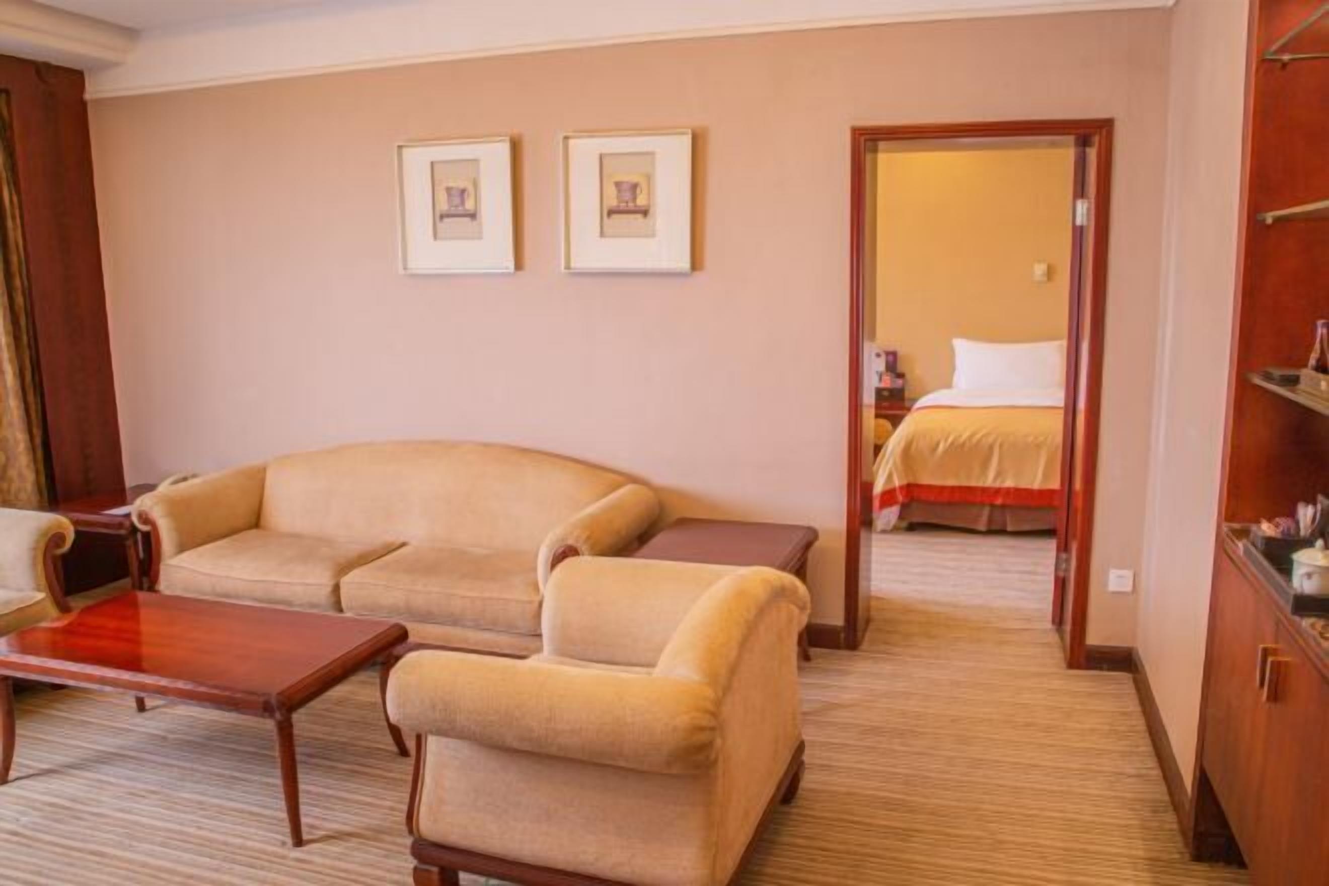A hotel room with a sofa, a small table, and a bed. There are two framed pictures on the wall.