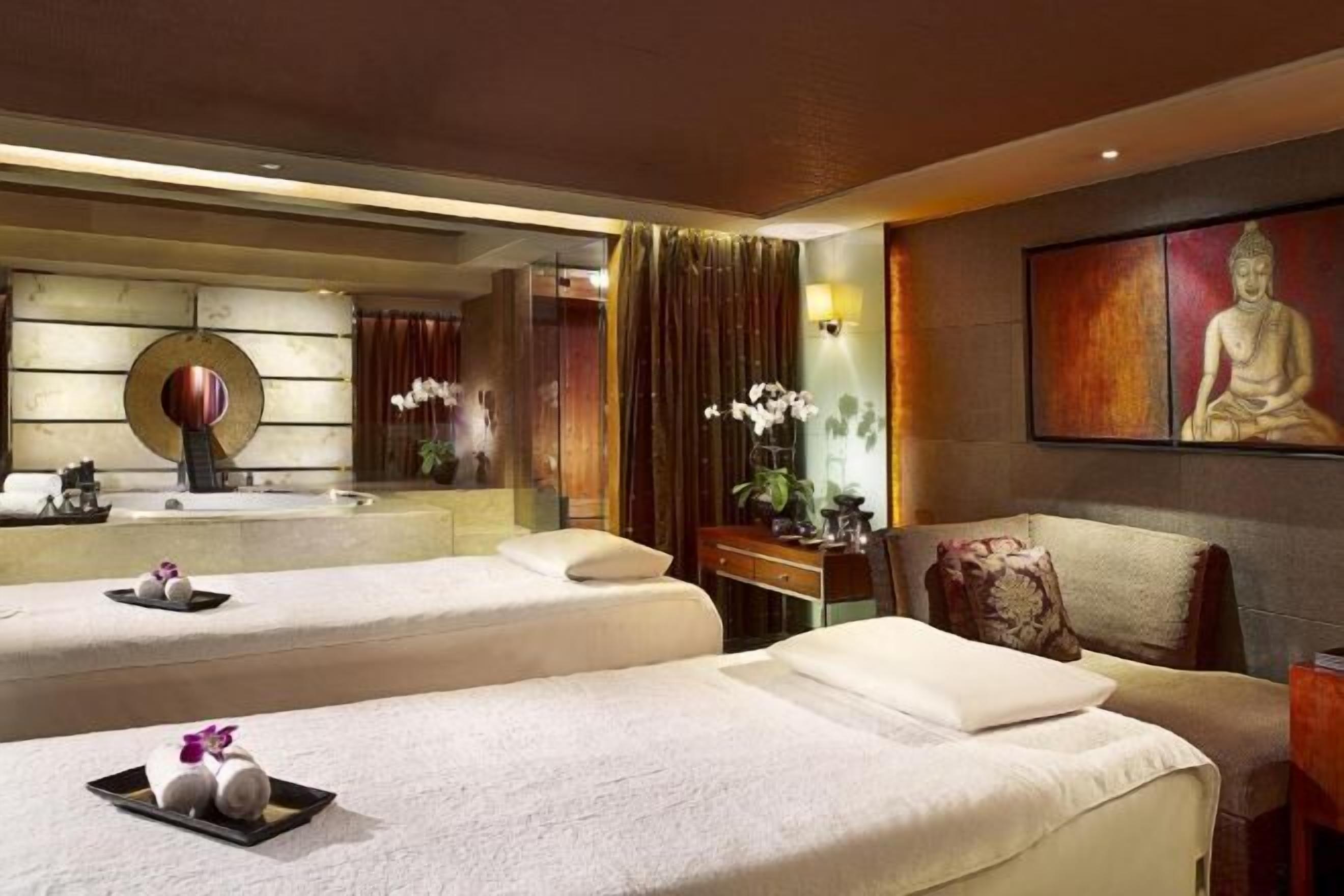 Ein Hotelzimmer mit zwei Betten, einem großen Spiegel, einer Buddha-Statue und einem kleinen Schreibtisch mit Lampe.