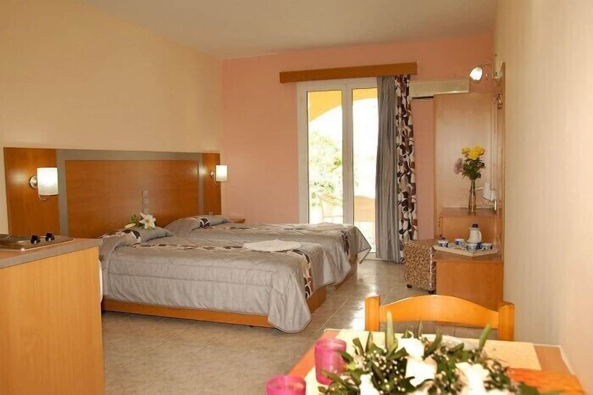 A hotel room with two beds, a small desk, a chair, a table with a vase of flowers, and a window with curtains.