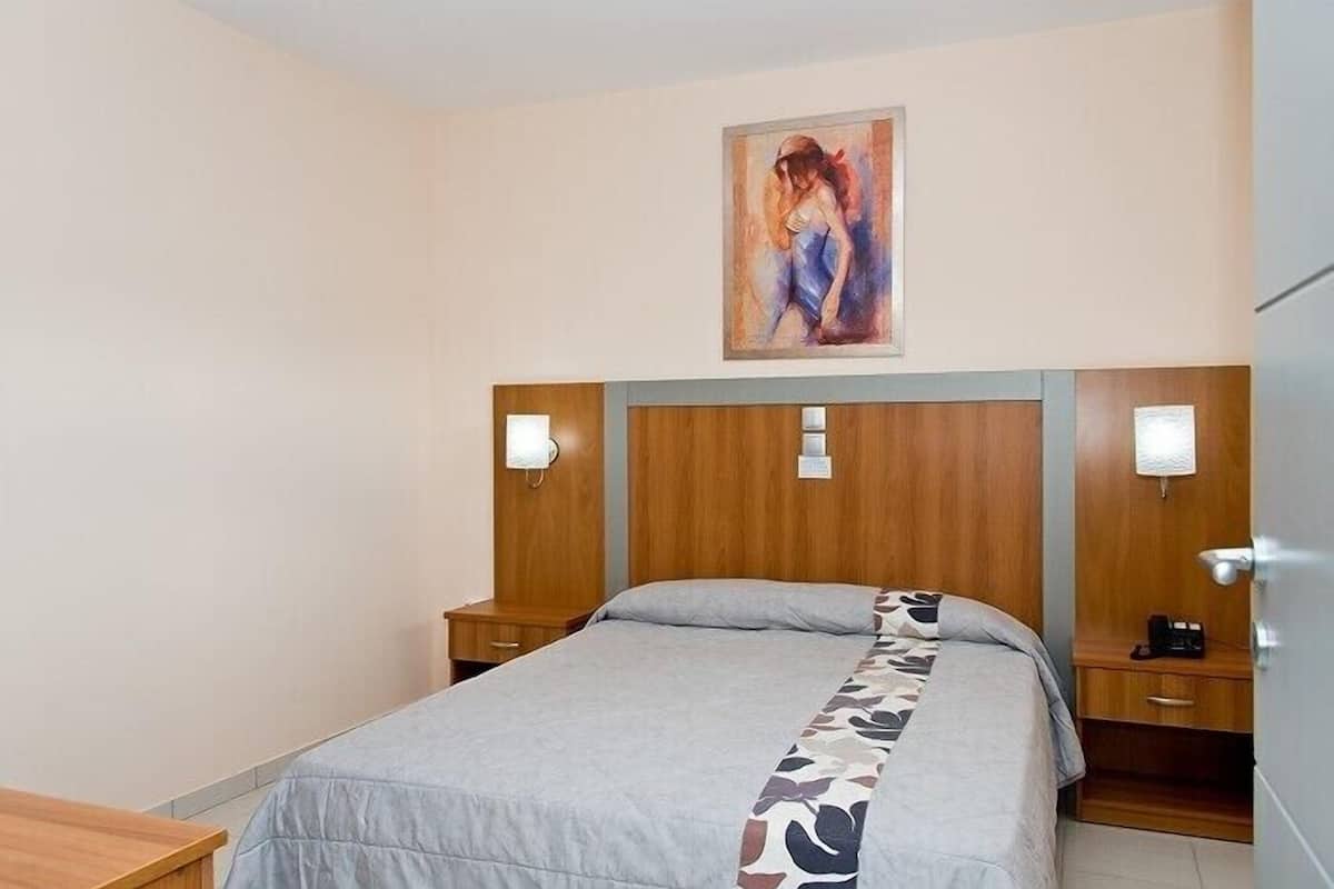 A hotel room with a bed, wooden headboard, bedside tables, and a painting on the wall.