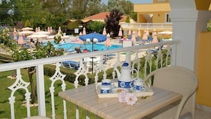 Un balcon avec une table préparée pour le petit-déjeuner, donnant sur un espace piscine agrémenté de parasols et de chaises longues.