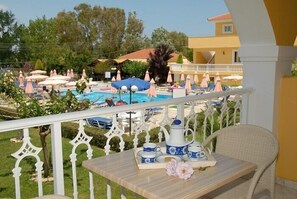 A balcony with a table set for breakfast, overlooking a pool area with umbrellas and lounge chairs.