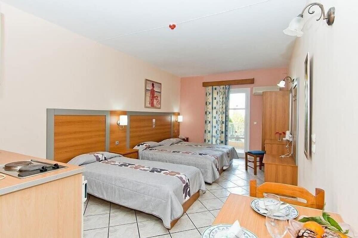 A hotel room with two beds, a dining table, a kitchen area, and a bathroom.