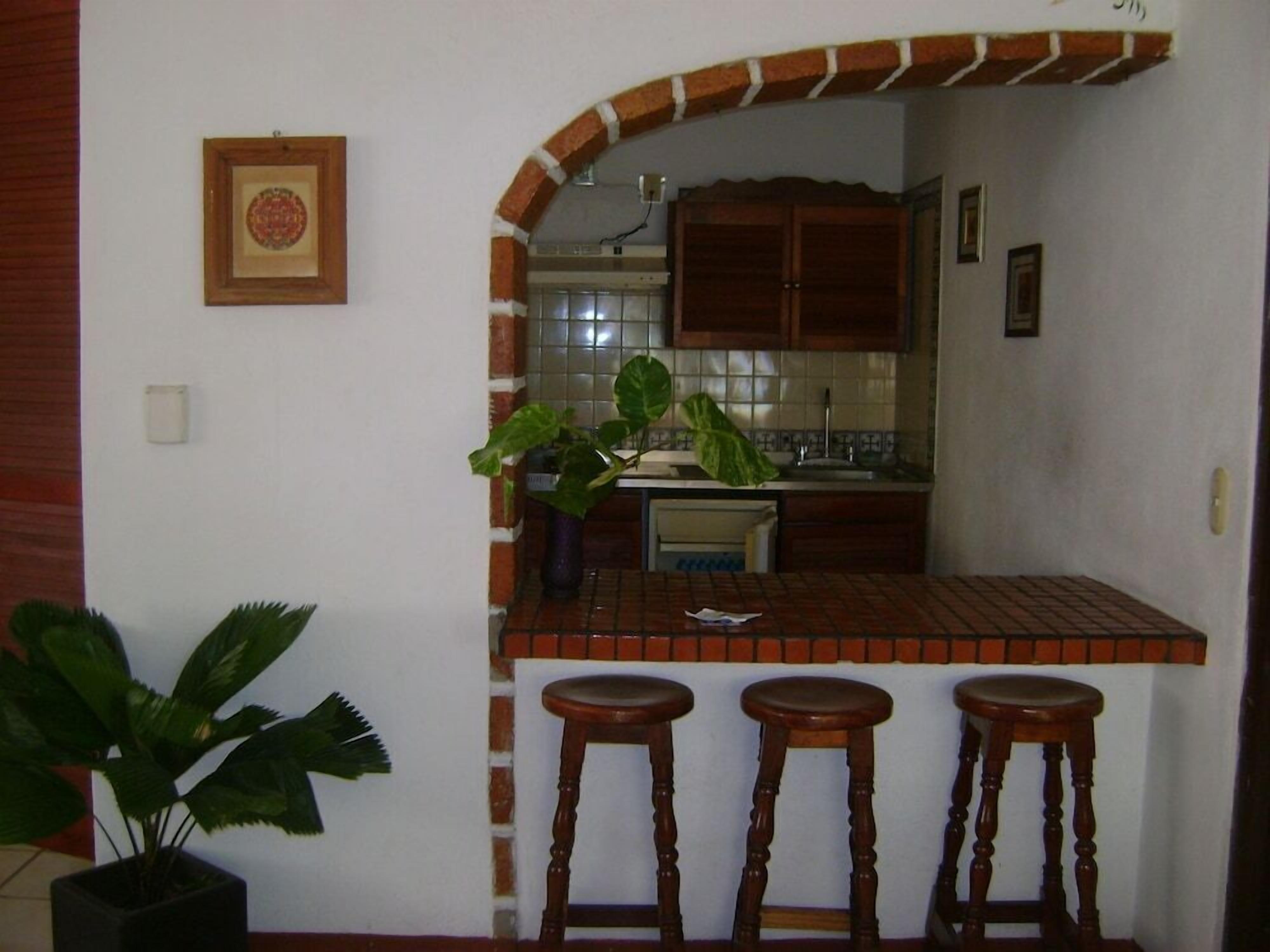Una cocina con salpicadero de azulejos, armarios de madera y tres taburetes.