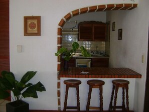 A kitchen with a tiled backsplash, wooden cabinets, and three stools. - Vallarta Sol (Puerto Vallarta)
