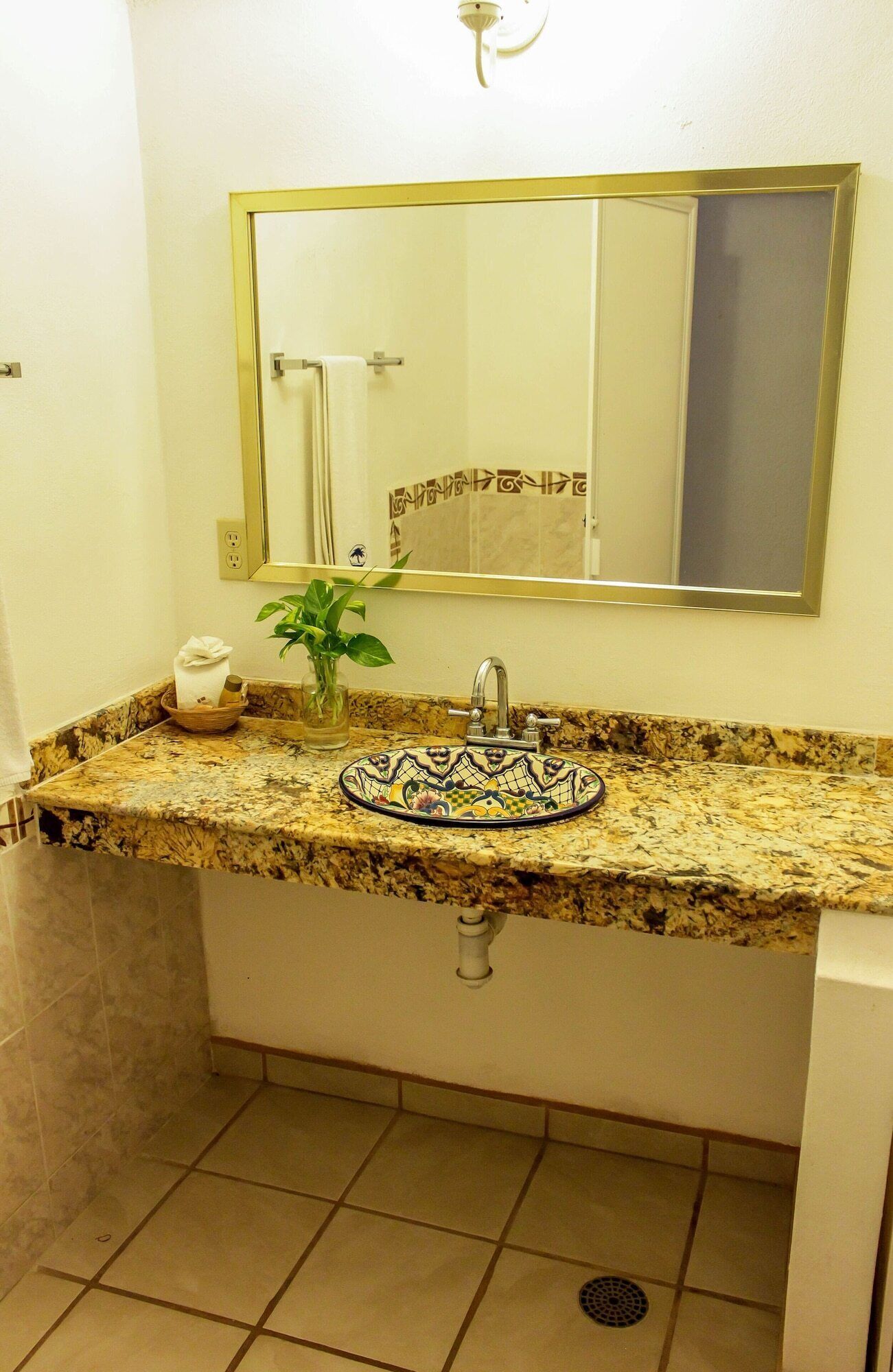 Une salle de bain avec un comptoir en granit, un lavabo orné de carreaux décoratifs, un miroir et un porte-serviettes.