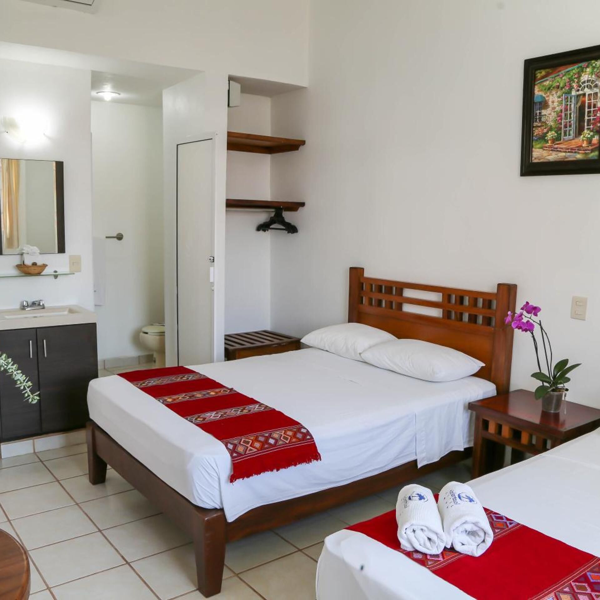 Ein Hotelzimmer mit Bett, Nachttisch mit Handtüchern, kleinem Tisch mit Pflanze, Spiegel, Schrank und einer Tür zu einem anderen Raum.