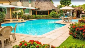 A swimming pool with a thatched-roof structure in the background, surrounded by outdoor seating and lush greenery. - Vallarta Sol (Puerto Vallarta)