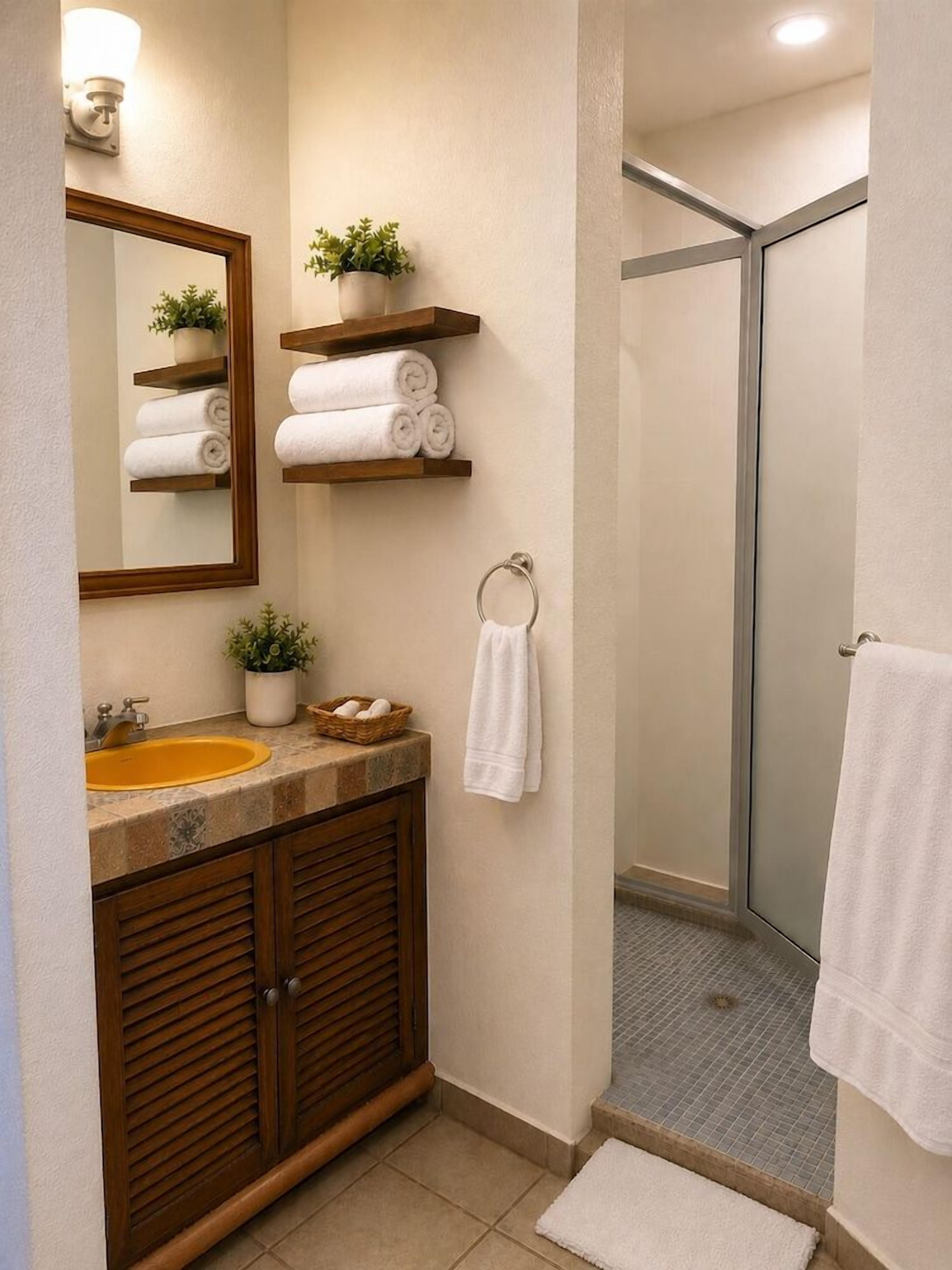 Een badkamer met een wastafel, spiegel, handdoekhouder, douche en houten kasten.