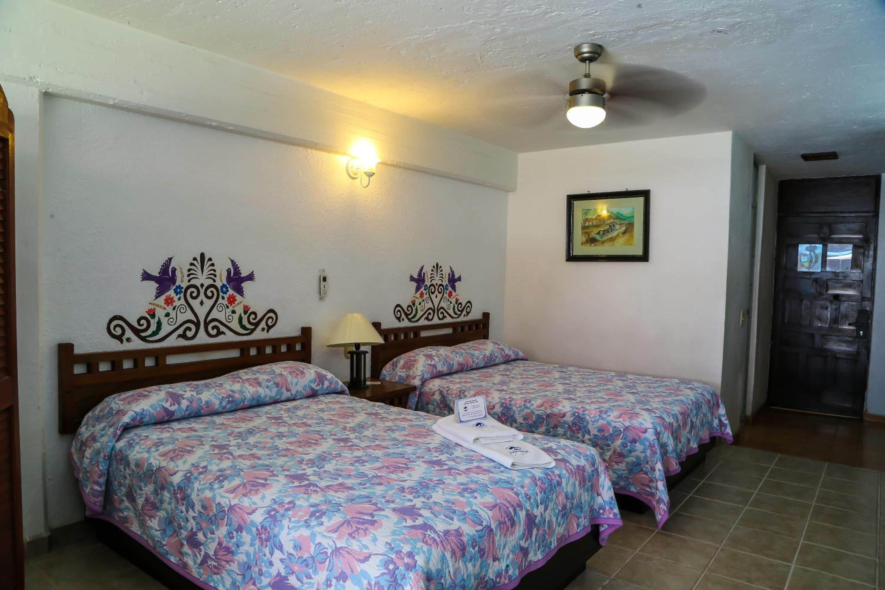 A hotel room with two beds, a ceiling fan, a wall-mounted light, and a framed picture.