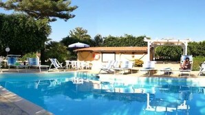 A swimming pool with lounge chairs and umbrellas, surrounded by greenery and buildings.