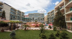 A hotel courtyard with multiple balconies, a central rock feature, and outdoor seating areas. - Sunny Day Club (Nessebar)