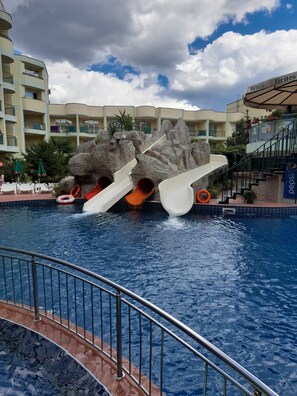 A swimming pool with a water slide, surrounded by a building with balconies and a Pepsi sign.