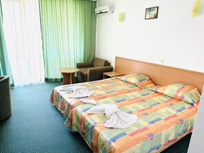 A hotel room with two beds, a small table, a chair, and an air conditioning unit on the wall.