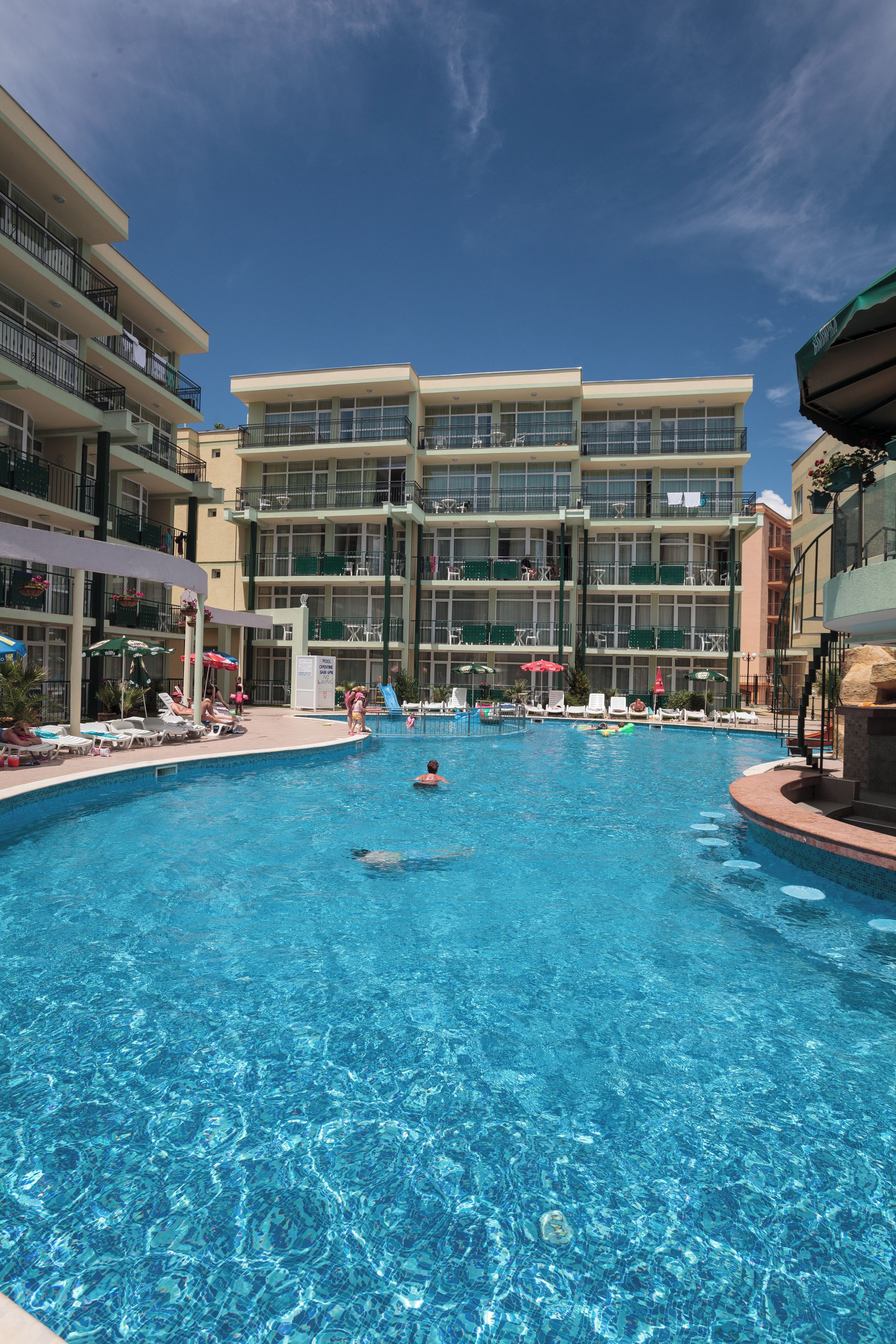 Un área de piscina de hotel con varios niveles de balcones, sillas de descanso y sombrillas.