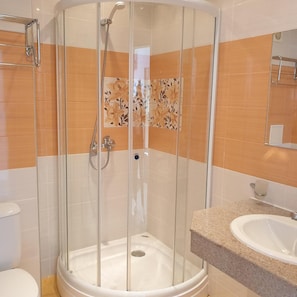 Un box de ducha con paredes de vidrio, un lavabo blanco y una encimera a la derecha.