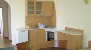 A compact kitchen with wooden cabinets, a white countertop, and basic appliances including a stove and microwave. - Sunny Day Club (Nessebar)