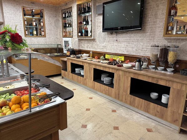 A buffet area with a variety of food options, a television mounted on the wall, and a brick wall design.