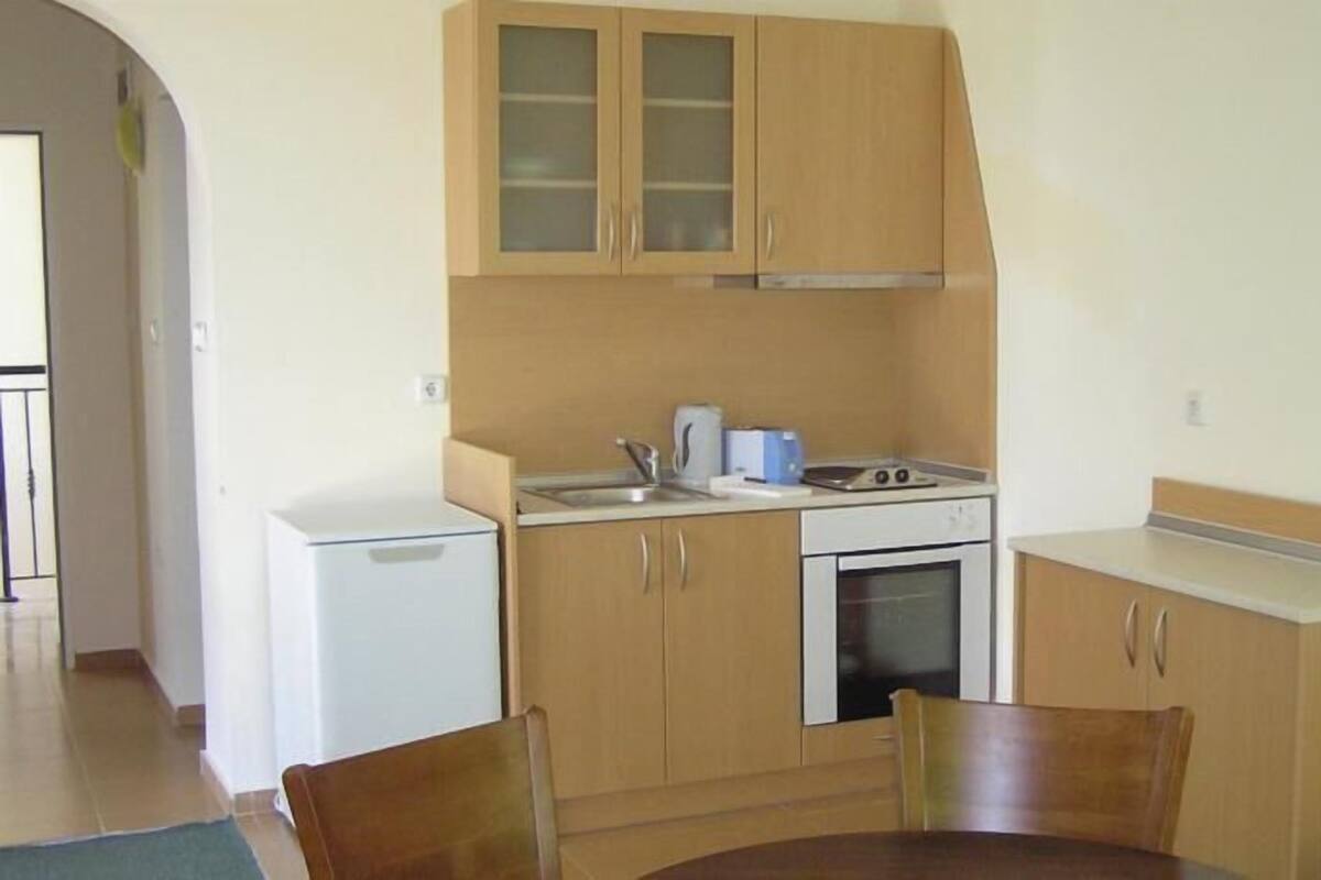 A compact kitchen with wooden cabinets, a white countertop, and basic appliances including a stove and microwave.