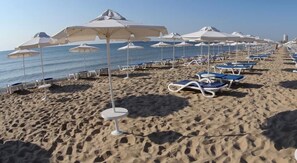 A beach with rows of sun loungers and umbrellas, a sandy shore, and the ocean in the background.