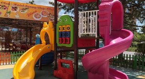 Un parque infantil con un tobogán amarillo, un tobogán en espiral rosa y una estructura de juegos con un letrero verde y amarillo.