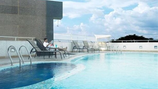 A swimming pool with lounge chairs and a person reading a book. - Hotel Satkar Residency (Thane)