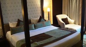 Relax in comfort with a plush bed and a cozy chair, surrounded by a stylish patterned wallpaper and natural light.