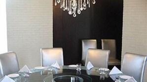 A round dining table with a glass top, surrounded by six chairs. - Hotel Satkar Residency (Thane)